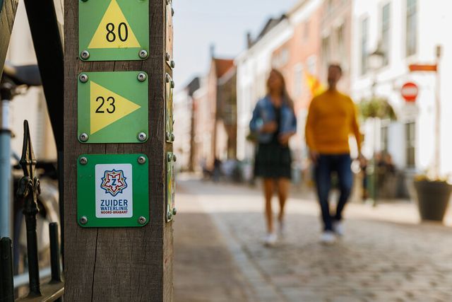Knooppunt paal Zuiderwaterlinie waar twee wandelaars langs lopen